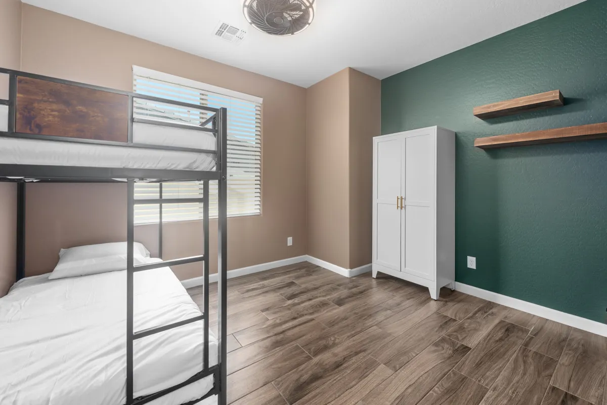 A cozy bunk room featuring a full-over-full bunk bed, a playful green accent wall, and a white wardrobe. The room is inviting and fun, designed for kids or extra guests to relax, play, or chat late into the night.