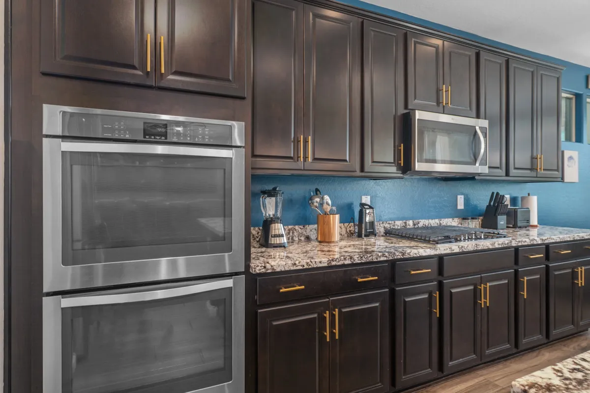 A cozy kitchen scene displaying dark cabinetry, a granite countertop, and stainless steel appliances. The space is well-organized and bathed in natural light, evoking a sense of warmth and modern comfort—perfect for cooking or gathering.
