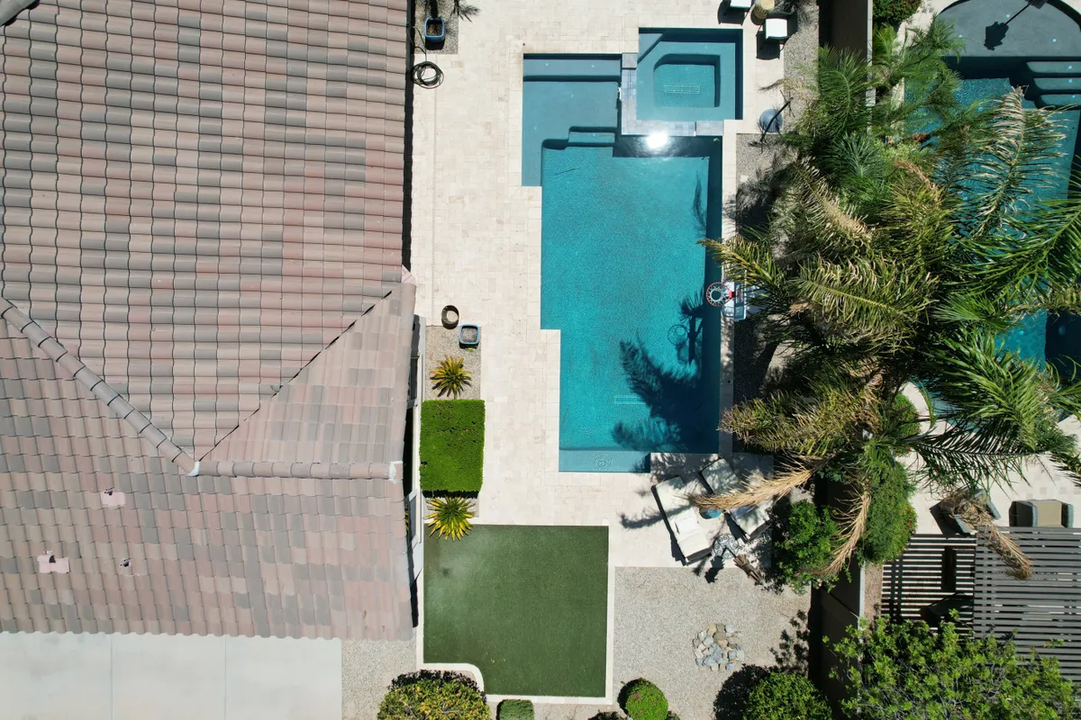 This exterior image captures the swimming pool and attached hot tub with palm trees and a spacious patio area. The pool looks inviting with sparkling blue water, and the hot tub is positioned adjacent, surrounded by comfortable seating. The scene suggests a tranquil, private retreat perfect for relaxing and social gatherings.