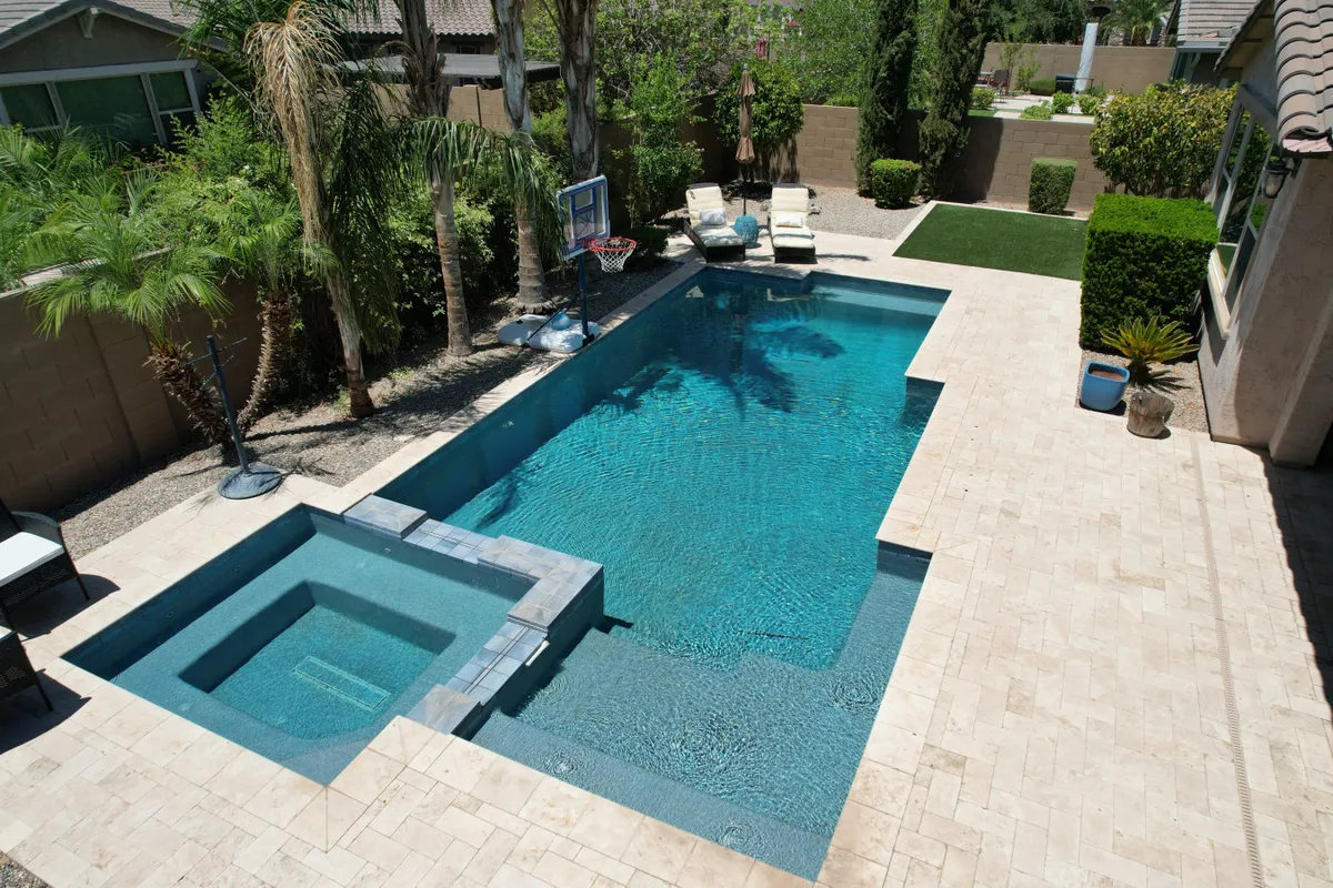 A vibrant backyard scene featuring a sparkling swimming pool, an inviting hot tub, several lounge chairs, a basketball hoop, and lush greenery all around. The space exudes a sense of relaxation and fun, ideal for group gatherings and outdoor activities.