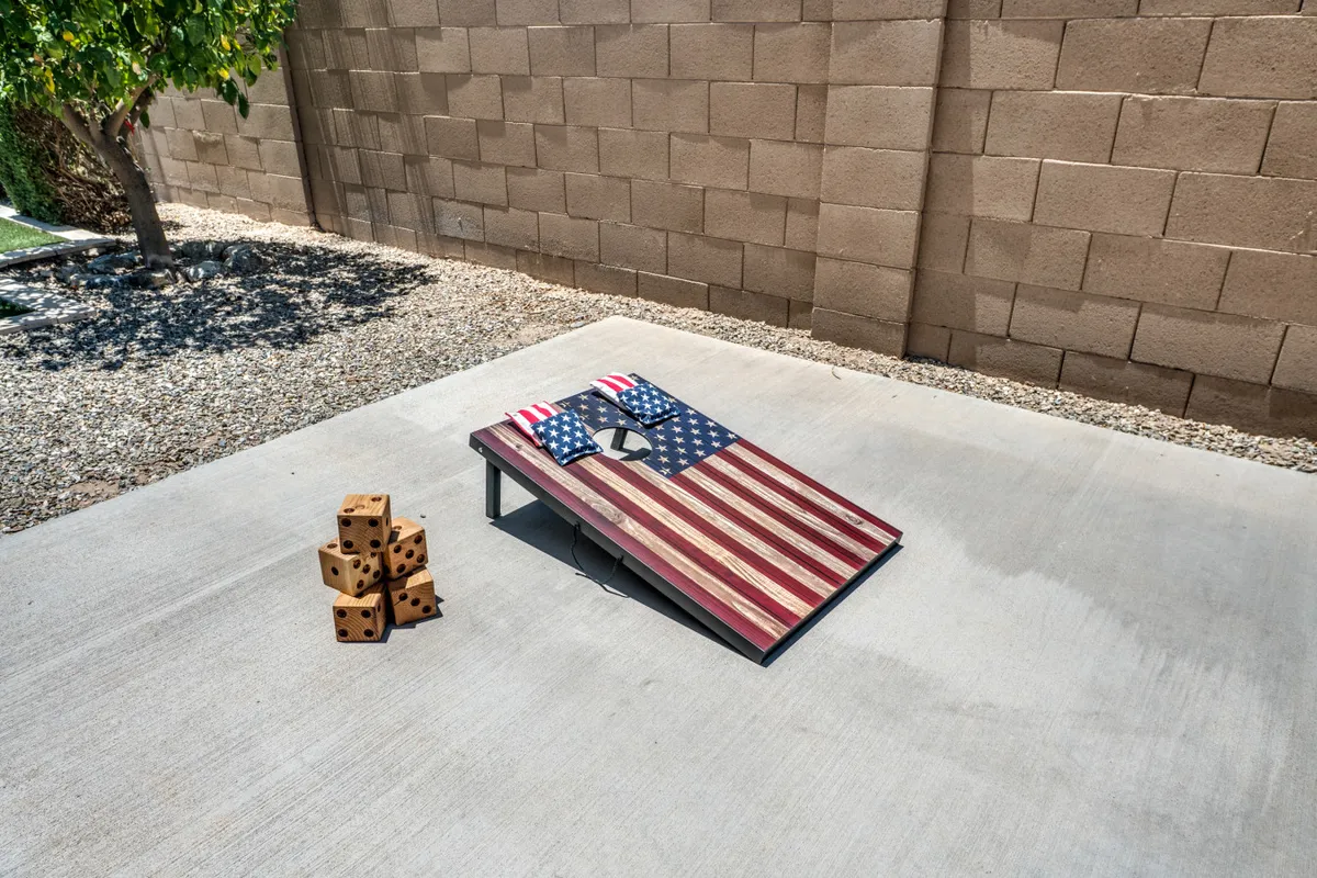 A playful outdoor setup with a cornhole board featuring an American flag design and a stack of dice, ready for friendly games. The scene exudes a relaxed, social atmosphere ideal for group bonding and backyard gatherings.