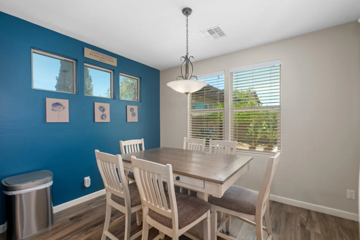 A warm and welcoming breakfast nook with a dining table, blue accent wall, chandelier, and windows that let in natural light. The intimate arrangement is perfect for morning coffee or quiet planning sessions.