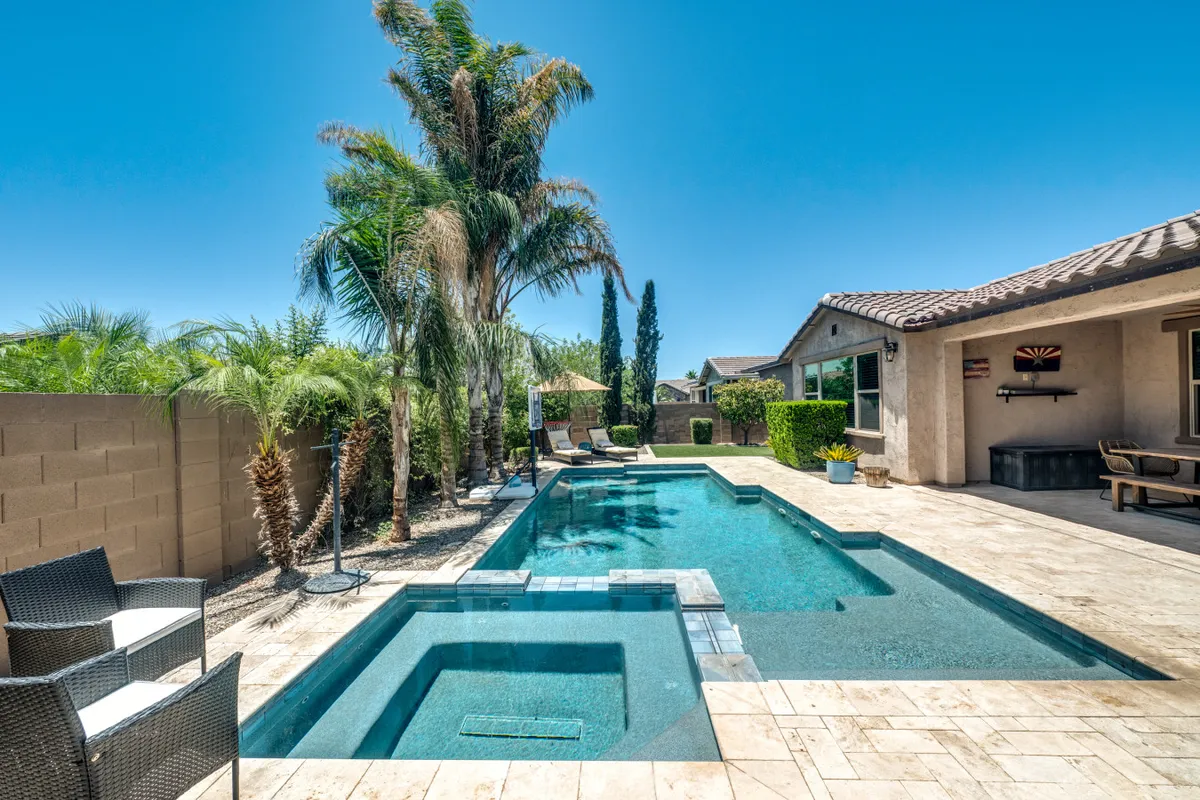 A stunning view of the home's backyard oasis at sunset, featuring a sparkling swimming pool, an inviting spa, swaying palm trees, and a spacious outdoor seating area. The scene is tranquil and luxurious, ideal for relaxing or celebrating after a big game.