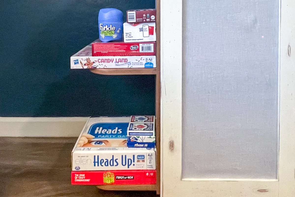 A playful and colorful shelf filled with board games, with game boxes neatly stacked and a textured cabinet door visible. The setup is ready for spontaneous fun and friendly competition.